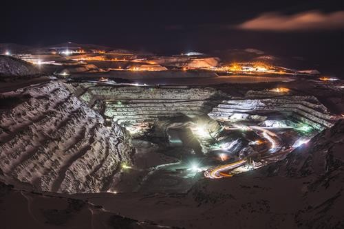 The Carol Lake open pit mine at night, lit by floodlights with truck light trails spiralling down the terraced walls