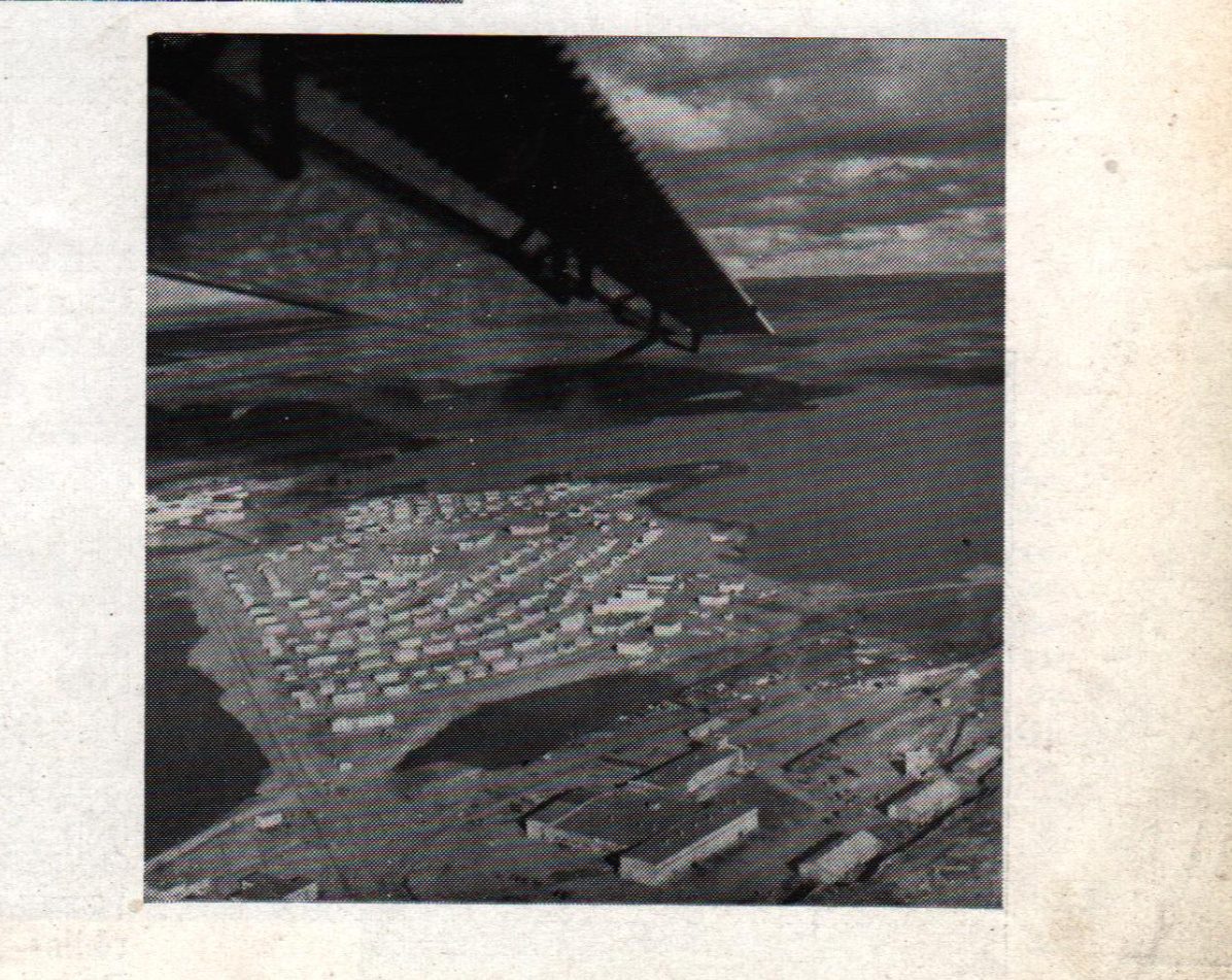 Aerial view of the Carol Lake construction camp taken from a bush plane in 1959, showing rows of trailers and barracks arranged on bare Labrador Shield beside the lake
